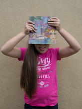 Load image into Gallery viewer, Girl holding The Elly Rose Adventures selfies from Townsville written and illustrated by Maggie O'Hara pulling a funny face and having fun