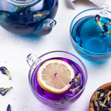 Load image into Gallery viewer, A glass pot of blue tea, and two glass cups of Fleur Tea. One with blue tea, one with purple tea.
